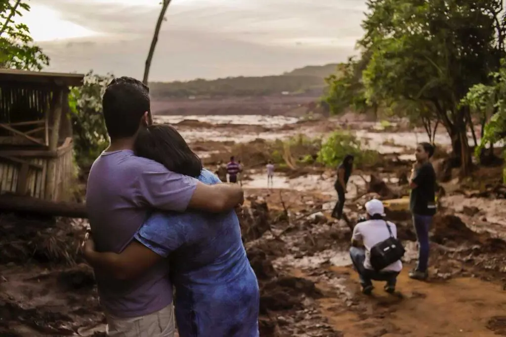 casal se abraçando olhando para terreno tomado por lama de barragem.