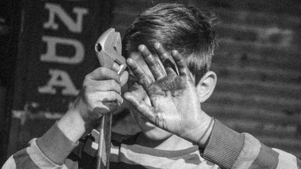 Imagem de uma criança com uma chave inglesa na mão cobrindo o seu rosto com a mão suja representando o abuso infantil e a exploração de crianças e adolescentes