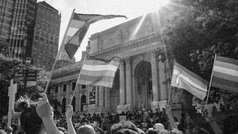 Imagem de um protesto com pessoas erguendo a bandeira LGBTQIAP+ lutando pela diversidade sexual no mundo e os direitos LGBT+