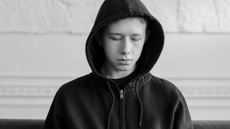 Imagem de um adolescente de jaqueta e capuz sentado e triste representando as medidas socioeducativas e os direitos das crianças e adolescentes