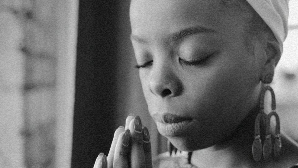 Imaegm de uma mulher negra com os olhos fechados e com as mãos em posição de oração representando os desafios do livre exercício da fé