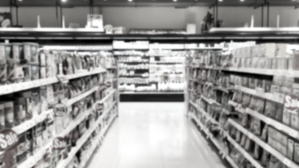 Corredor de um supermercado com prateleiras à esquerda e à direita, representando a diversidade de produtos que são taxados por meio dos impostos sobre consumo.