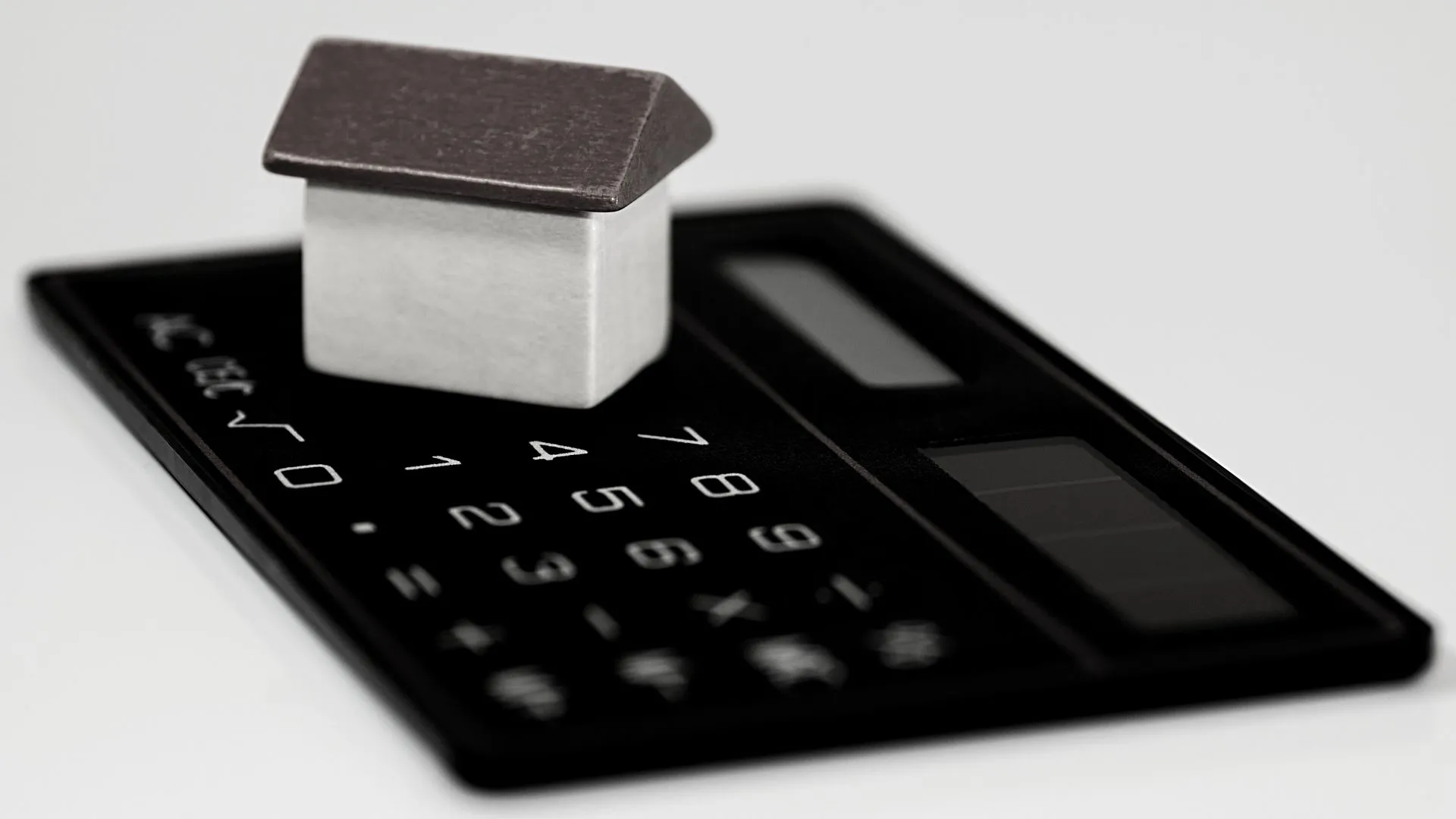Imagem em preto e branco com uma casinha de madeira sobre uma calculadora para representar as cobranças de IPTU.