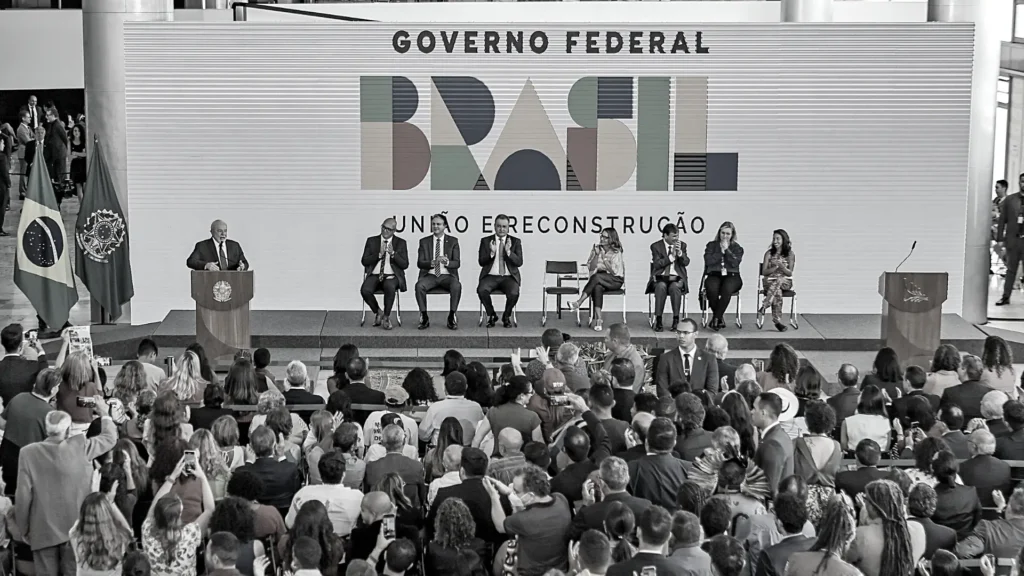 Imagem em preto e branco com multidão acompanhando a cerimônia de lançamento do novo bolsa família, política pública implementada pelo presidente Lula.