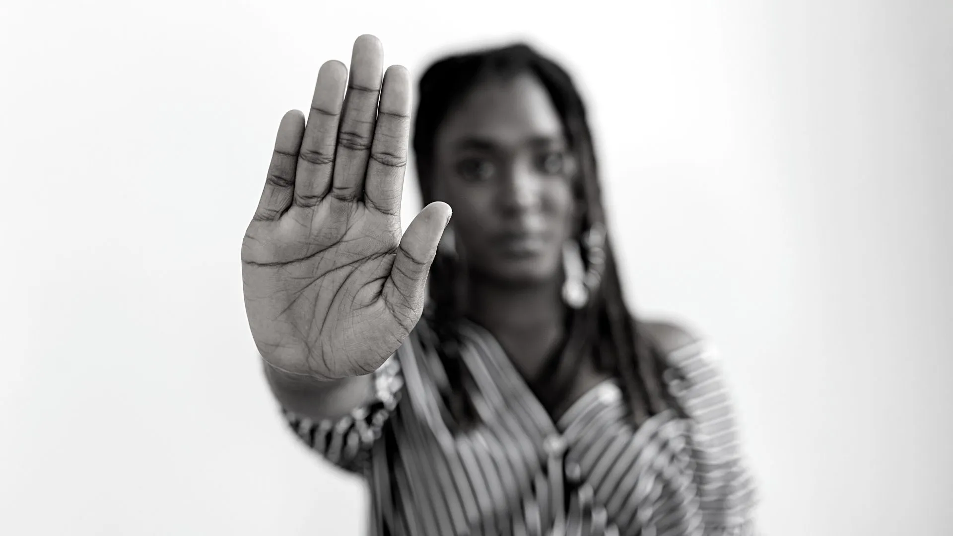 Imagem em preto e branco com mulher negra fazendo sinal de pare com a mão direita para simbolizar a necessidade de combater a desigualdade social.