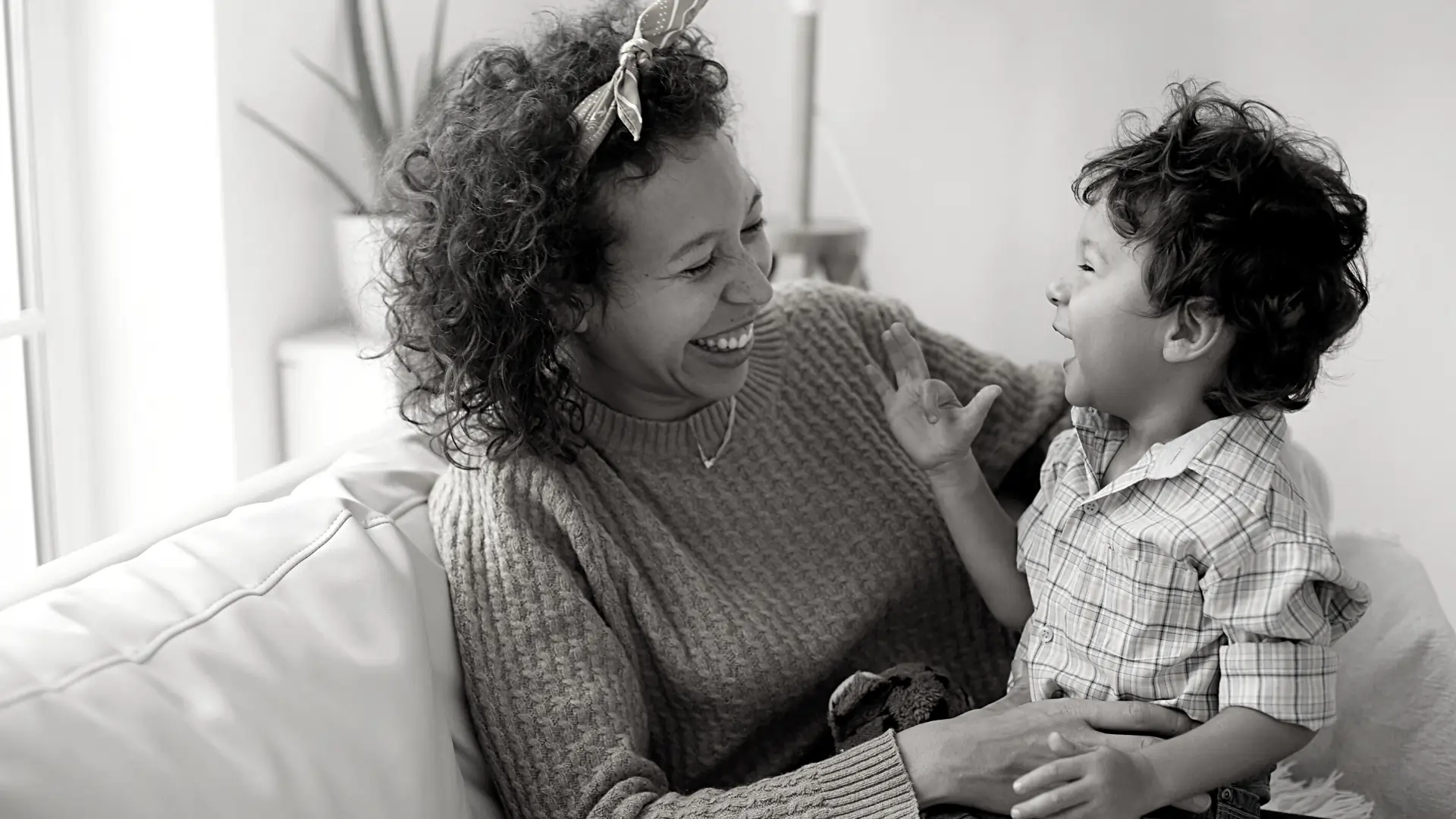 Imagem em preto e branco, mãe e filho estão sentados no sofá sorrindo, representado como a desigualdade de gênero foi promovida pela pensão alimentícia. 