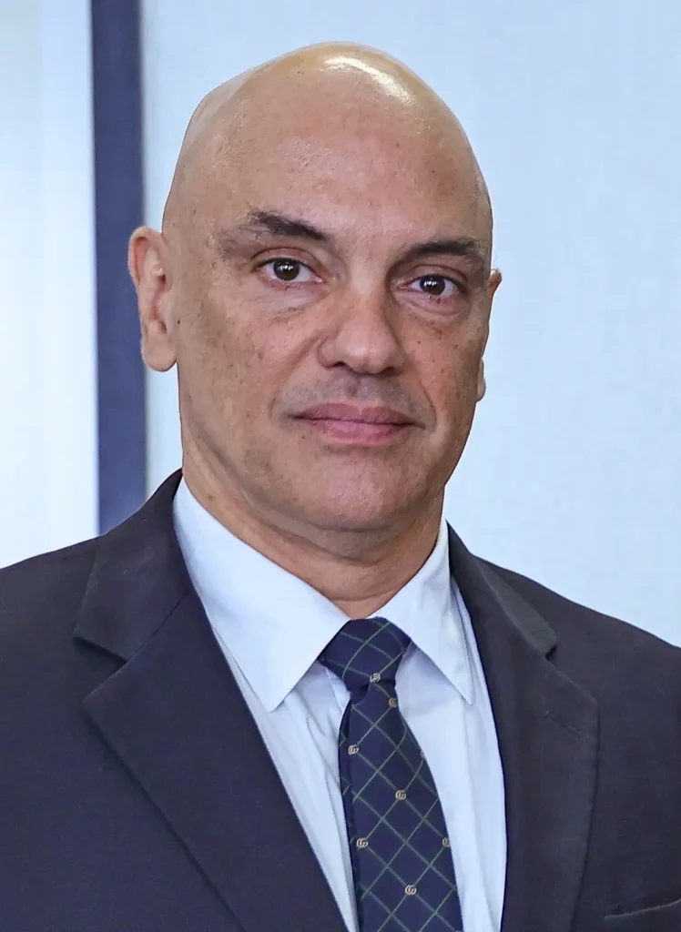 Homem careca de perfil, vestindo uma beca, em frente ao microfone com feição séria. Se trata do ministro Alexandre de Moraes. Texto sobre inquérito das milícias digitais.