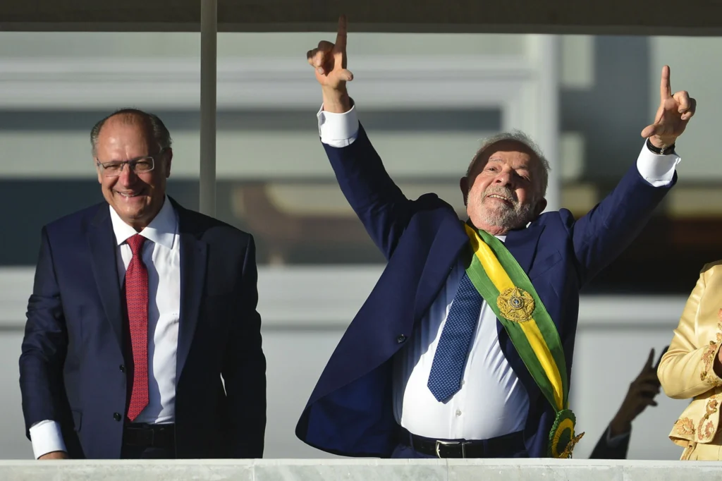 Dois homens brancos em carro oficial do governo, em pé, durante a posse presidencial