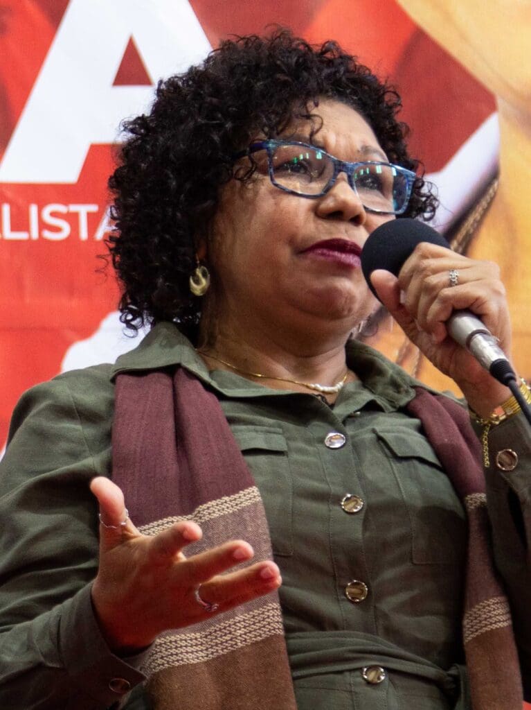 Mulher adulta negra discursando com um microfone na mão.