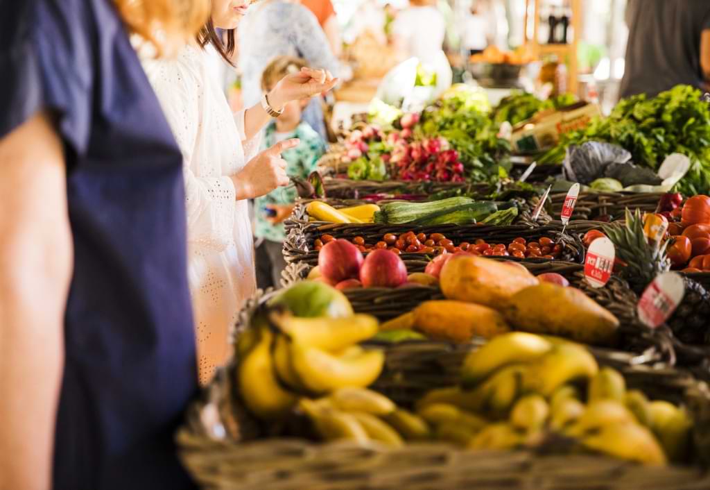 imagem com pessoas atrás de uma mesa com muitas frutas, verduras e legumes