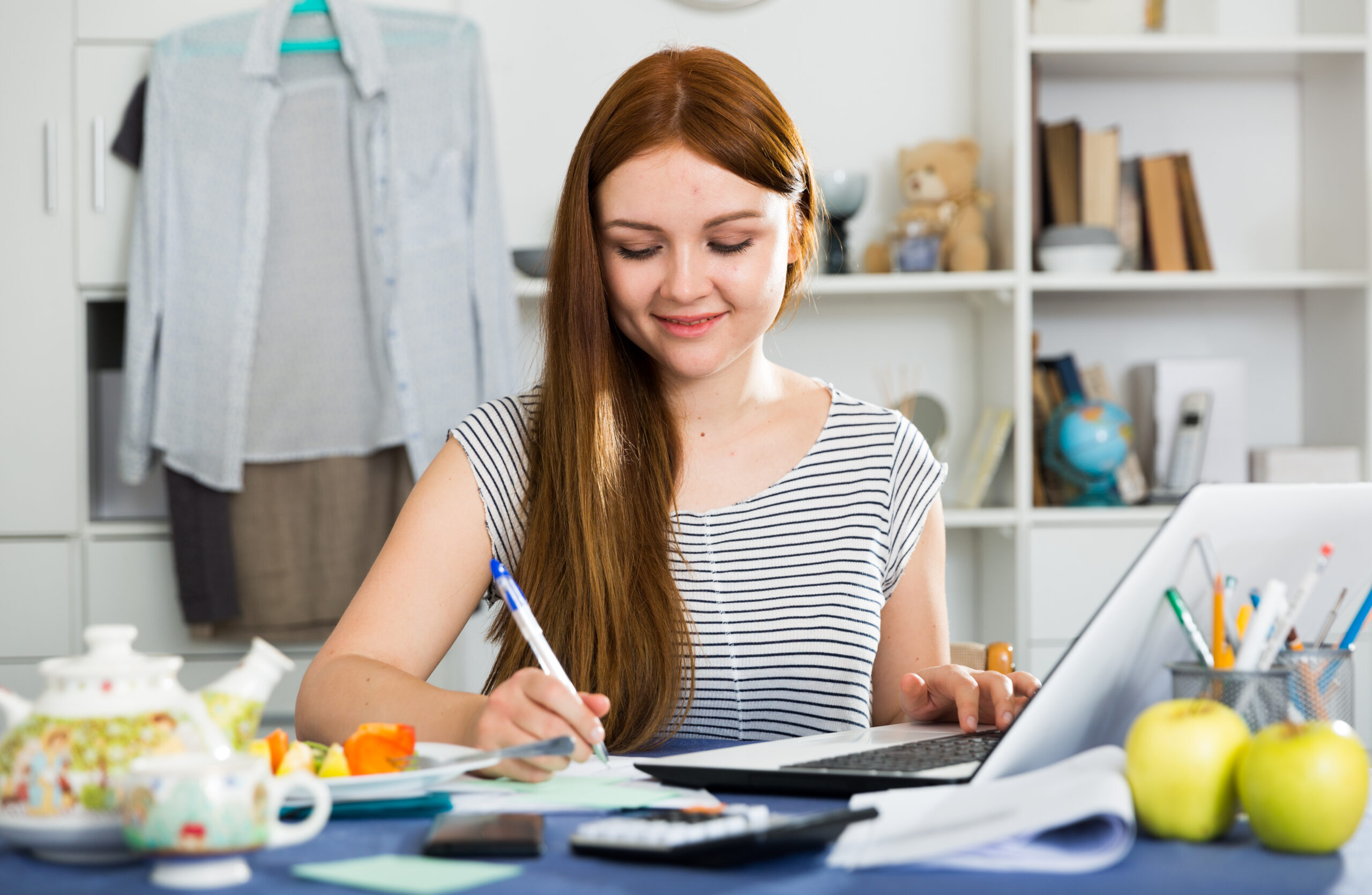 Young woman is sitting with laptop and documents at the table