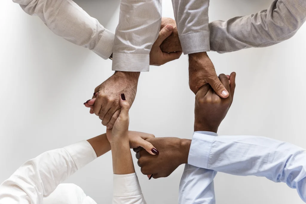 Pessoas de diferentes raças com as mãos dadas em um fundo branco, representando união e luta conjunta.