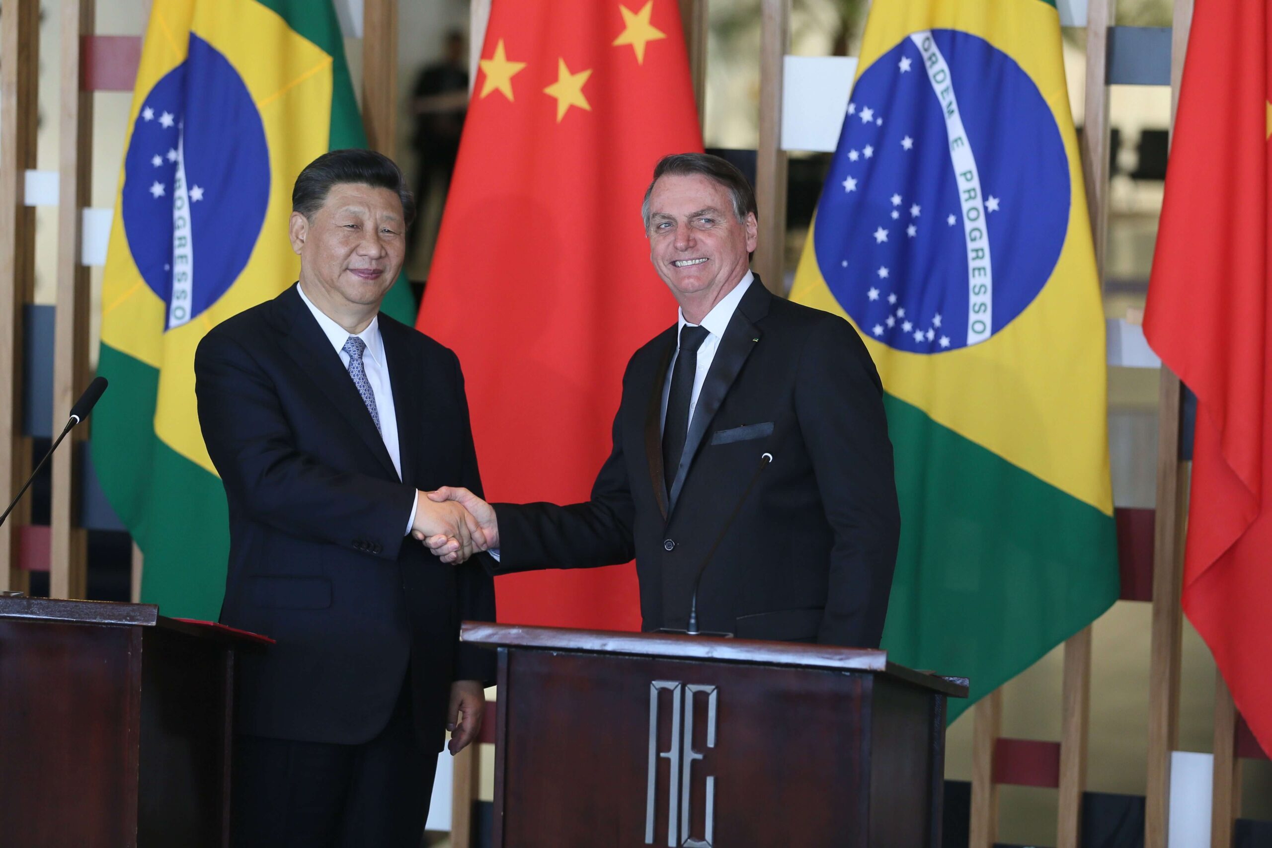 Presidente Bolsonaro em encontro com o presidente chinês Xi Jinping apertando as mãos. Conteúdo sobre comércio Brasil-China.