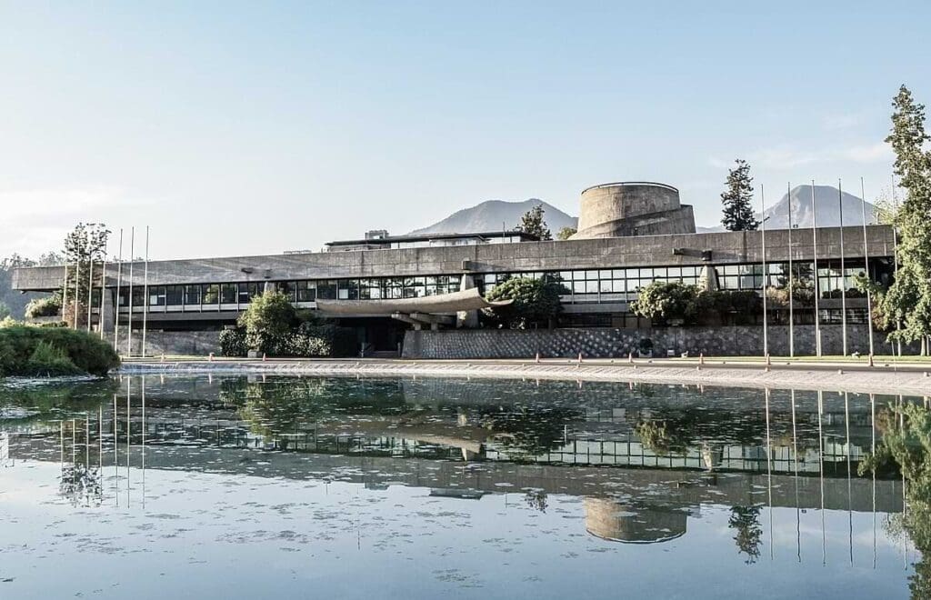 Foto de edifício plano cinza, com uma lagoa refletindo na frente 