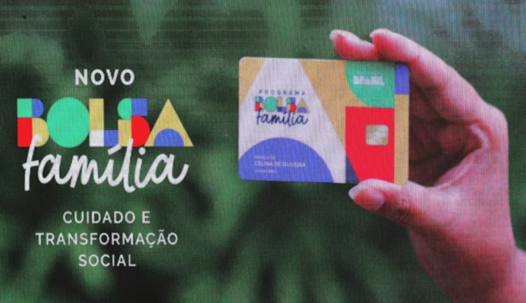 Imagem colorida, em primeiro plano, uma mão segura o cartão do Programa Bolsa Família, informando o novo programa que busca transformação social.