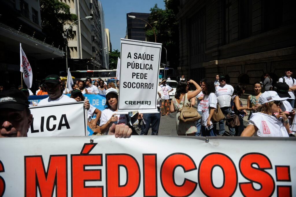 Pessoas em protestos pela saúde segurando ma placa "a saúde pública pede socorro". Conteúdo sobre Judicialização da saúde no Brasil.