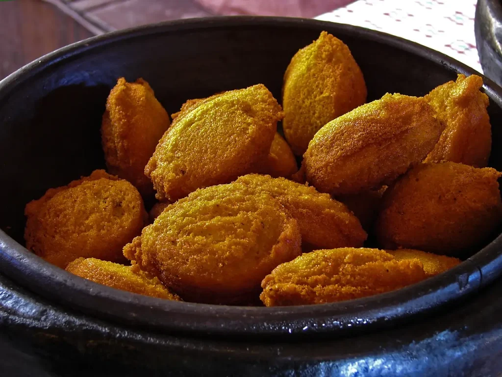 Uma tigela de alimentos fritos, acarajé, repousa sobre uma mesa.