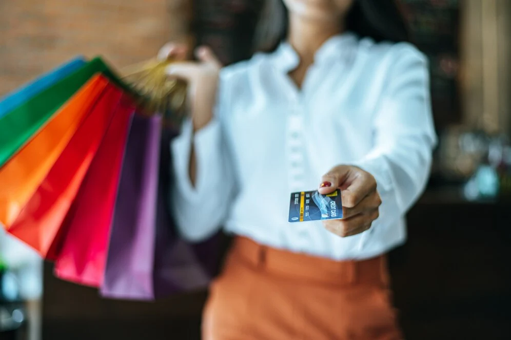 Mulher segurando sacolas e um cartão de crédito, consumindo tranquilamente, com seus direitos garantidos pelo Código de Defesa do Consumidor.