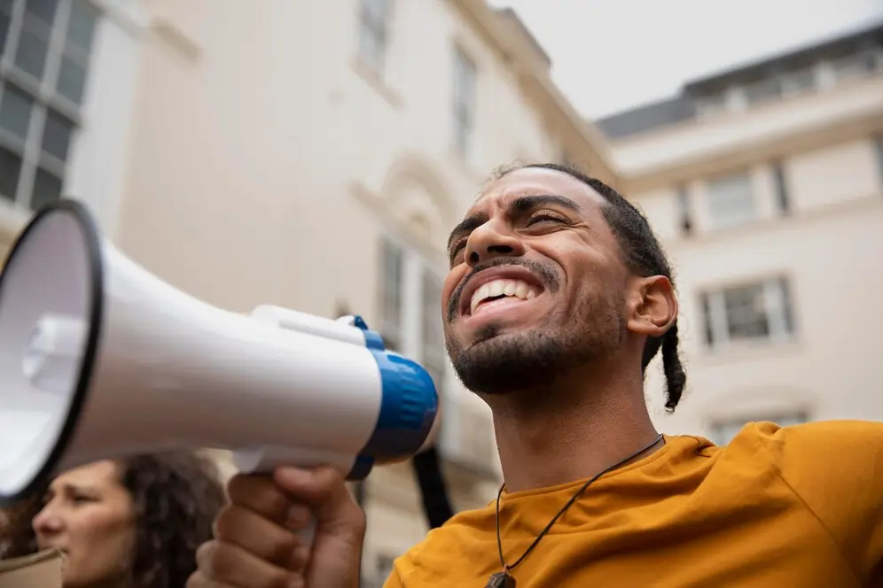 Homem negro com megafone na mão em uma rua. Texto sobre o que o candidato a vereador não pode fazer em ano eleitoral.