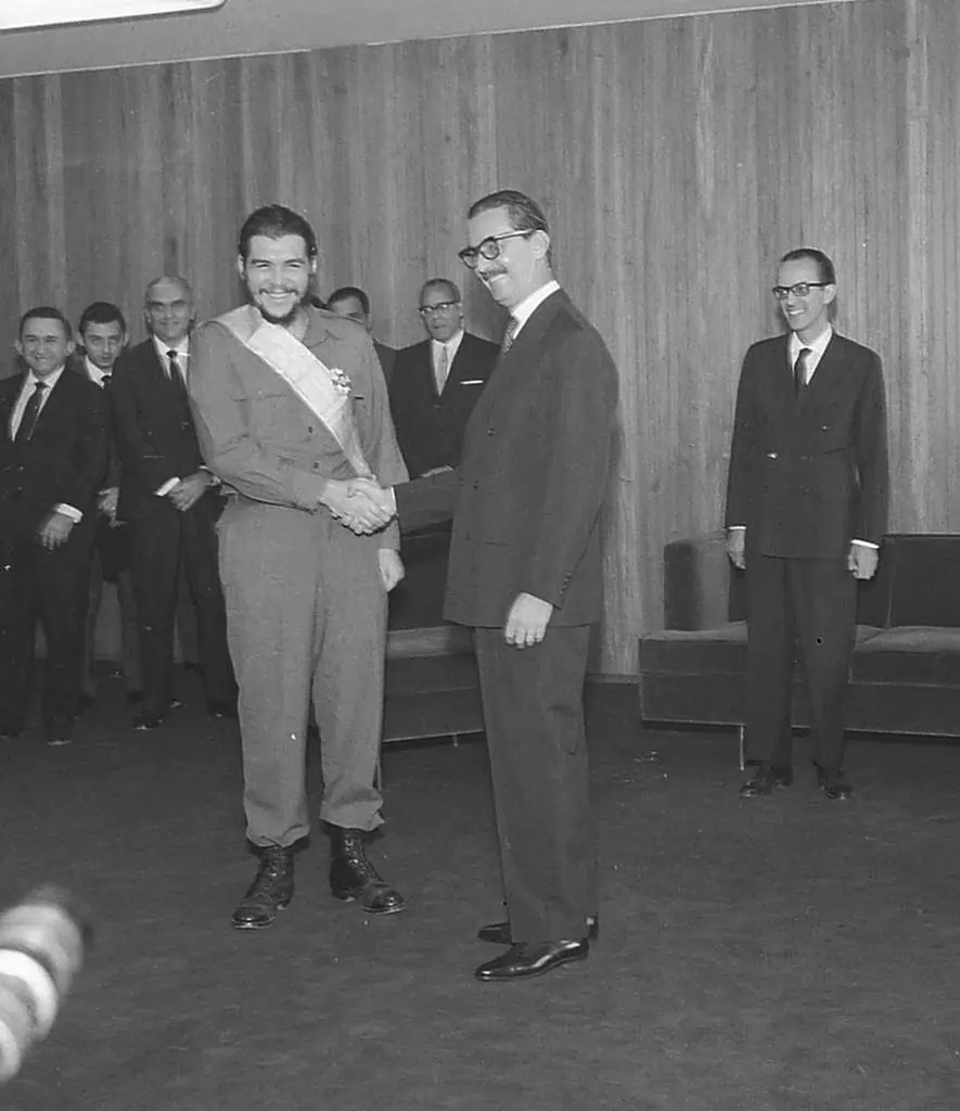 Na imagem, dois homens apertado a mão e sorrindo. Alguns outros homens atrás observando, a maioria sorrindo também. Todos estão em traje formal, e um dos homens que aperta as mãos está com uma faixa cruzando seu corpo. Texto: Jânio Quadros: o que levou o presidente a renunciar em sete meses?