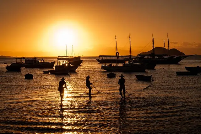 Imagens de pescadores na beira da praia em um pôr do sol, com barcos ao fundo. Texto: PEC das praias: privatização das praias?