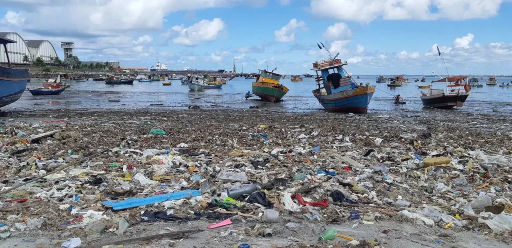 Foto de uma praia com muitos dejetos na areia. Texto: PEC das praias: privatização das praias?