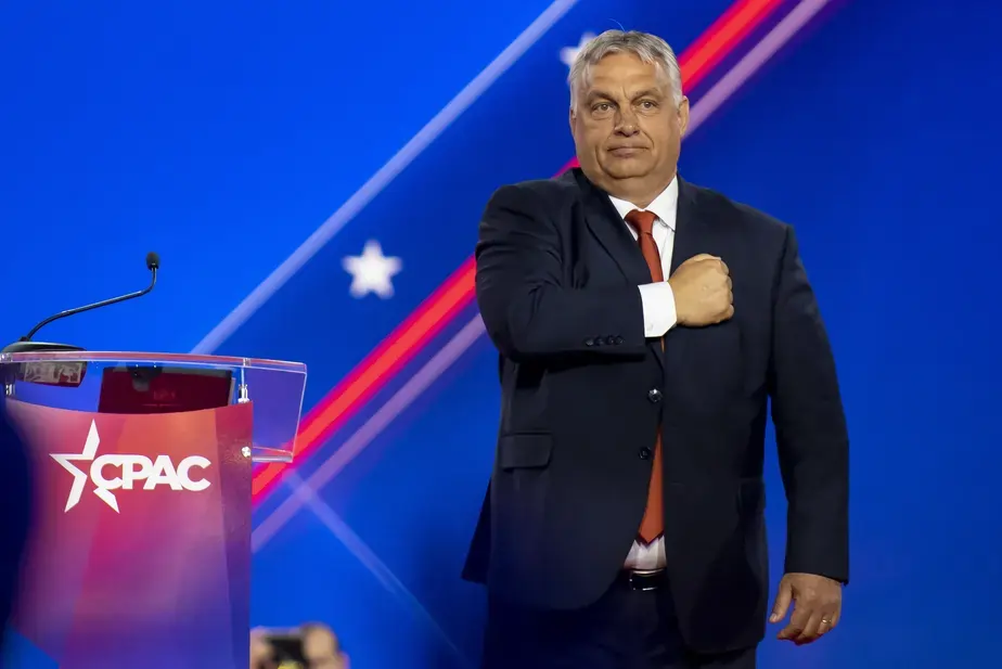 Na imagem, Viktor Orbán, um homem branco, de cabelo grisalho curto, aparência de idade um pouco avançada, com a mão em forma de punho junto ao peito, em sinal de lealdade. Está em cima de um palanque e olha para seu público. Texto: Entenda o conceito de autocracia eleitoral