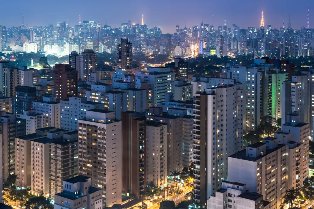 Imagem de prédios, com luzes acesas, em uma cidade, a noite. Texto: Fundos Imobiliários no Brasil: benefícios, riscos e como investir