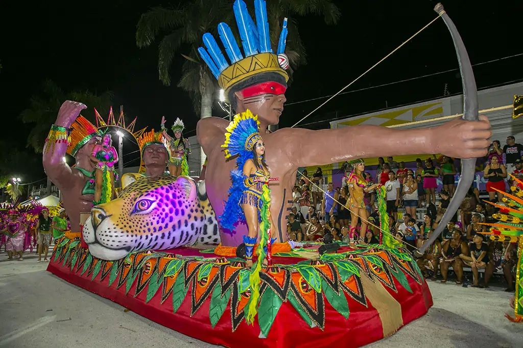 Imagem de uma alegoria com a representação de um indígena apontando uma flecha. 