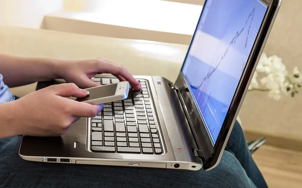 Pessoa sentada mexendo em computador apoiado no colo e segurando um celular com a outra mão. Texto: Meio ambiente de trabalho: uma proteção constitucional ao trabalhador