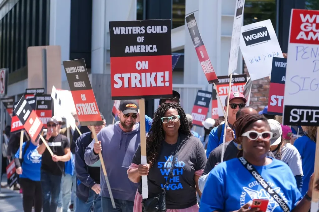 Imagem de pessoa protestando, com placas na mão, em defea de escritores de roteiro de Hollywood. Texto: O uso da Inteligência Artificial nas dublagens: perigo ou avanço?